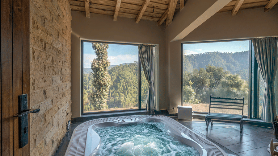 Indoor jacuzzi with bubbling water set against a stone-clad wall, below a timber ceiling, with large windows over forested hills at The Chamomile Estate.