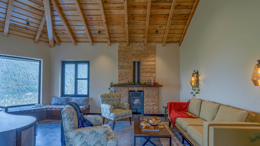 First floor lounge with a stone fireplace and wood stove, a cream sofa, floral armchairs and a window seat over the hills at The Chamomile Estate.