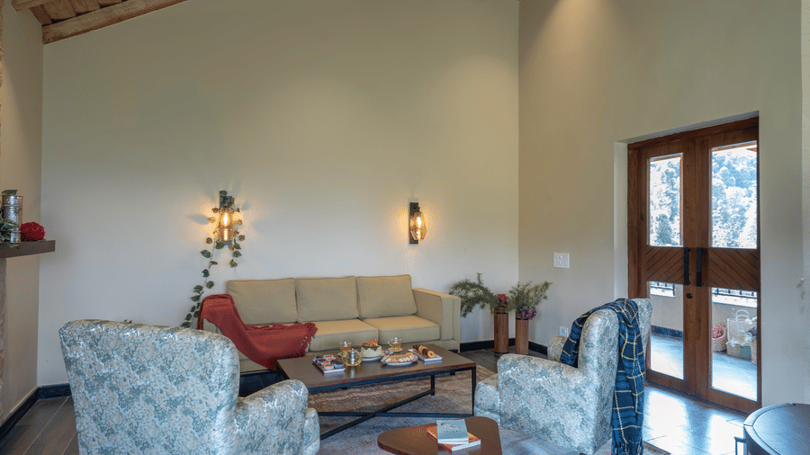 First floor lounge with a cream sofa, floral armchairs, a low table set with tea and snacks and glazed doors to the terrace at The Chamomile Estate.