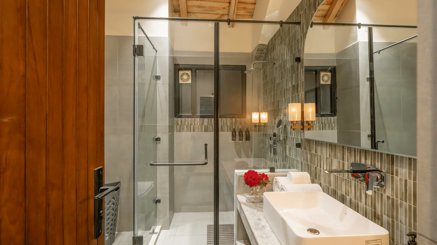 Oolong Room bathroom with a glass-enclosed rain shower, mosaic tiling, twin wall lights and a white basin on a marble counter at The Chamomile Estate.