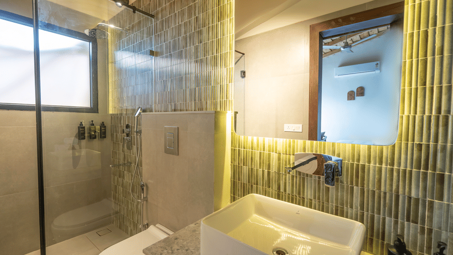 Sage Room bathroom with a walk-in glass shower, ribbed olive tiling, a backlit mirror and a rectangular basin on a stone counter at The Chamomile Estate.