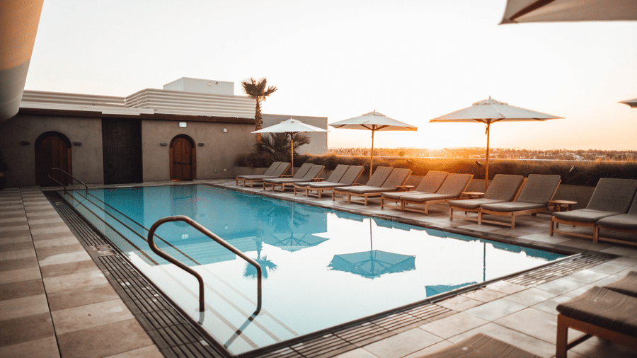 A swimming pool with loungers next to it and the sun setting in the background - The Cindrella Hotel, Siliguri