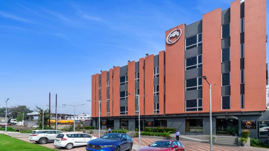 A modern hotel building with orange and grey exterior under a clear blue sky, with several cars parked in front | The Citi Residenci Hotel Banskopa