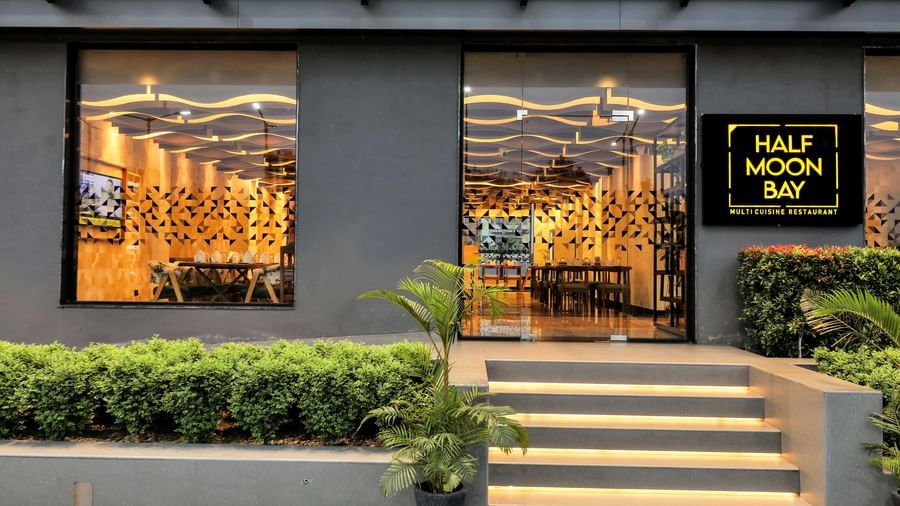 The exterior of a restaurant named Half Moon Bay with illuminated windows showcasing the interior and a neon sign | The Citi Residenci Hotel Banskopa
