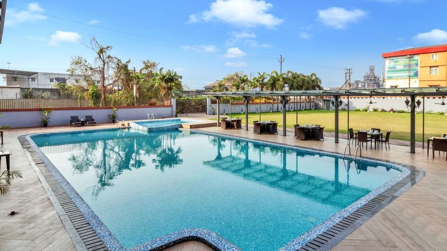 A large outdoor swimming pool with clear blue water, surrounded by lounge chairs and covered seating areas on a sunny day | The Citi Residenci Hotel Banskopa