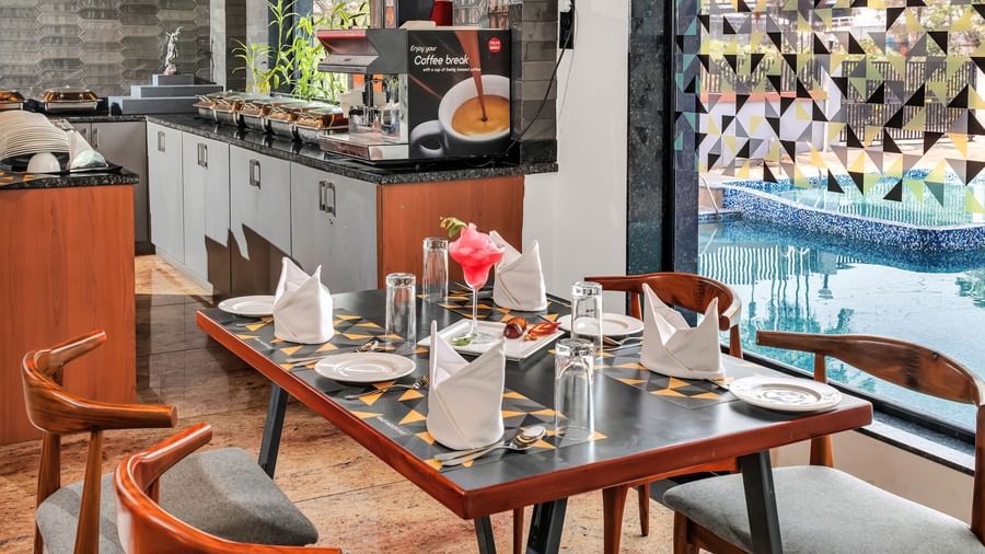 A restaurant dining area with set tables and chairs, overlooking a swimming pool through a glass wall  | The Citi Residenci Hotel Banskopa