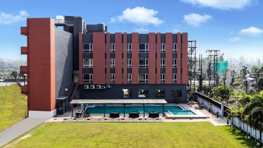 A modern hotel building with a swimming pool and green lawn under a partly cloudy sky | The Citi Residenci Hotel Banskopa
