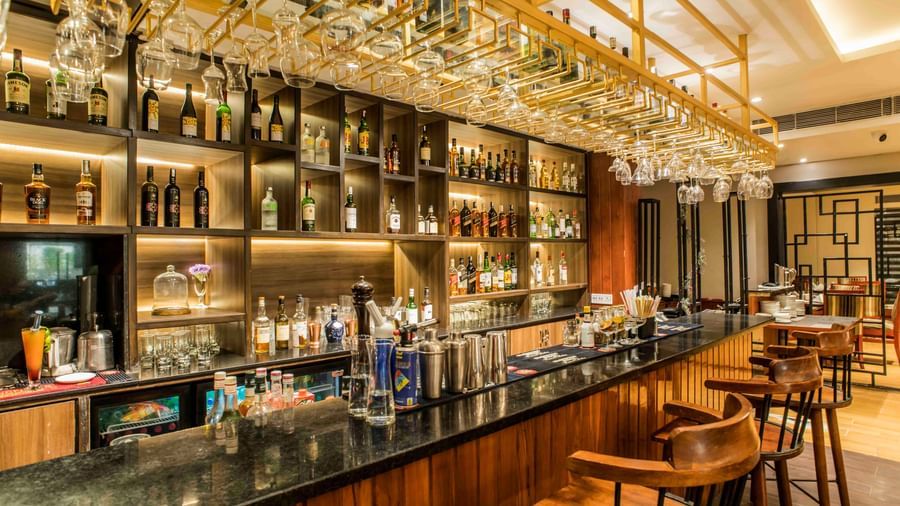 Well-stocked hotel bar with a dark countertop, multiple stools, and illuminated liquor bottles | The Citi Residenci Hotel Durgapur