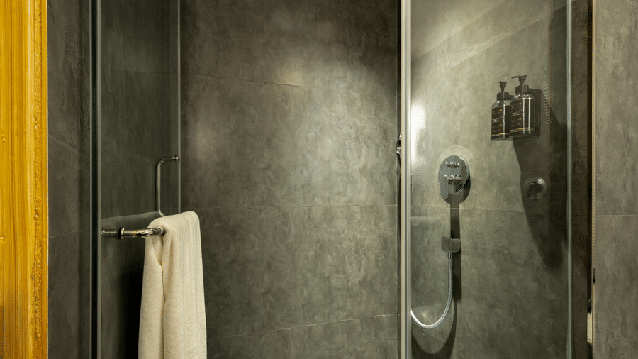 A walk-in shower with grey stone-effect walls and a glass partition at The Citrine, Bangalore.