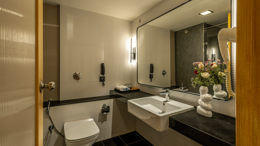 A bathroom vanity with a white rectangular sink, a large wall mirror, and a white toilet at The Citrine, Bangalore.