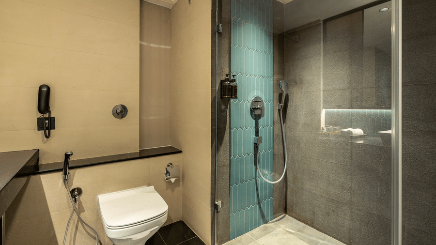 Club Room bathroom at The Citrine, Bangalore, with a glass-enclosed walk-in rain shower, blue mosaic feature wall, wall-hung WC and toiletries.