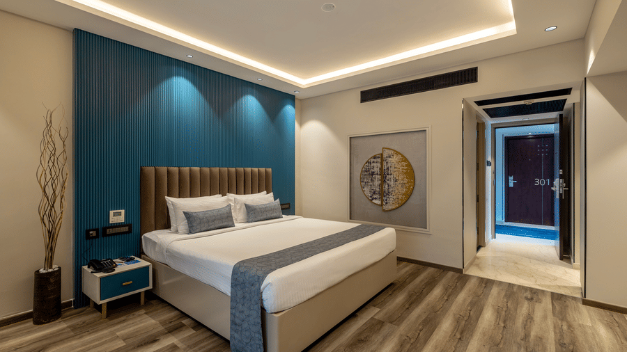 A double bed with a striped headboard against a blue textured wall and a doorway leading to a hall at The Citrine, Bangalore.