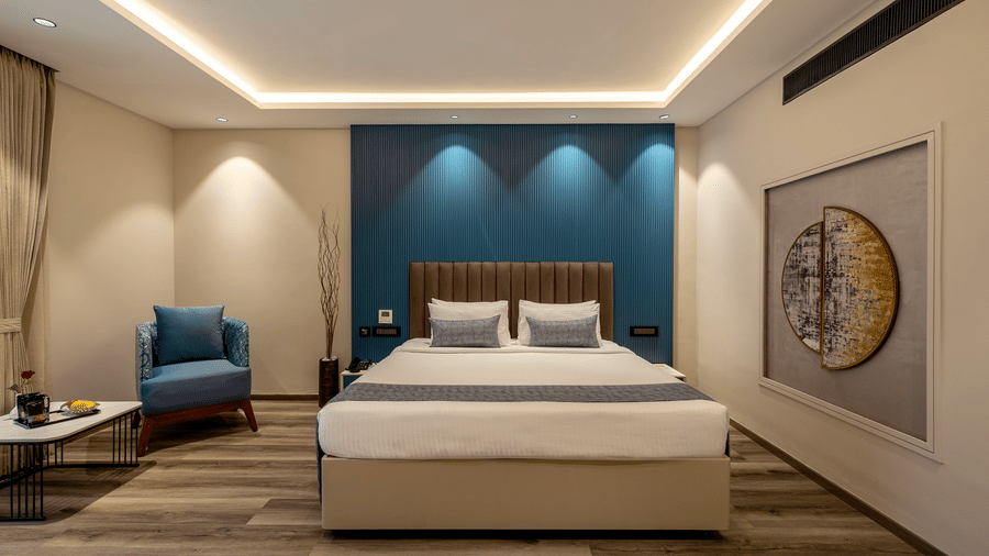 Club Room at The Citrine, Bangalore, with king bed, blue fluted headboard wall, accent armchair, round wall art, and warm cove lighting.