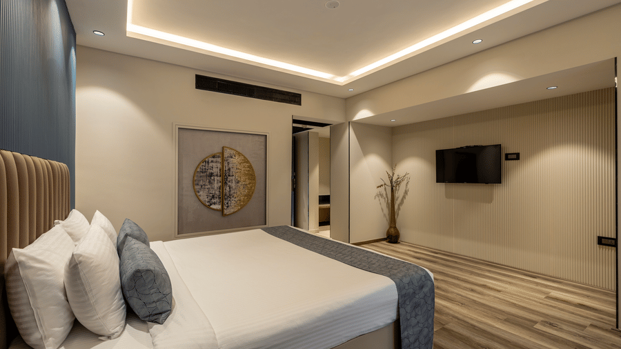 Club Room at The Citrine, Bangalore featuring a king bed with beige headboard, wall-mounted TV, framed circular artwork, and cove lighting.