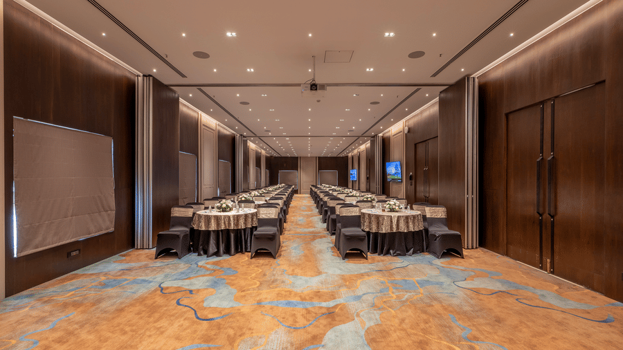 A large conference hall with long rows of tables and chairs on a patterned orange and blue carpet at The Citrine, Bangalore.