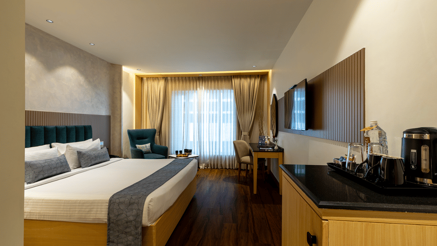 Executive King Room at The Citrine, Bangalore, with a king bed, teal armchair, wall-mounted TV, work desk, kettle and tray of refreshments.