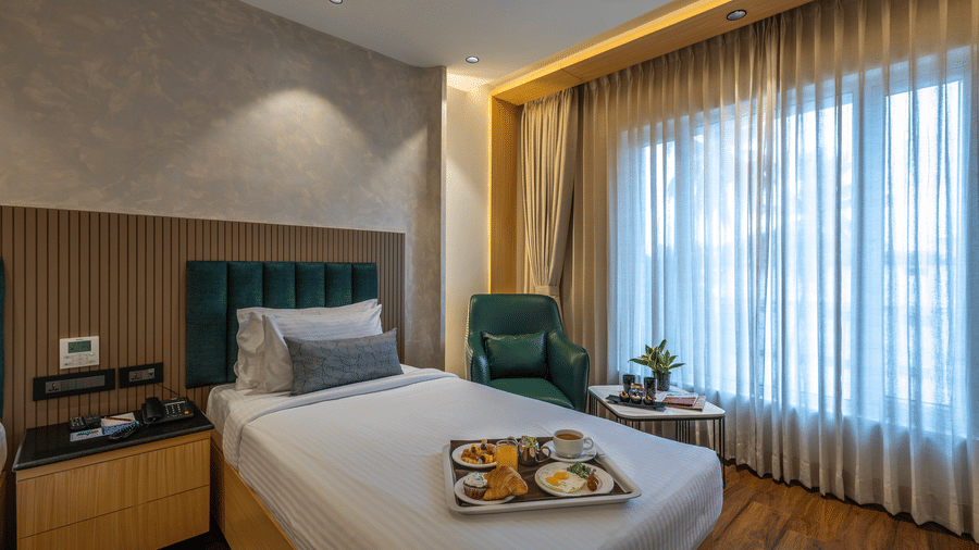 Executive Twin Room at The Citrine, Bangalore, with a single bed, green headboard, breakfast tray, armchair, and floor-to-ceiling sheer curtains.