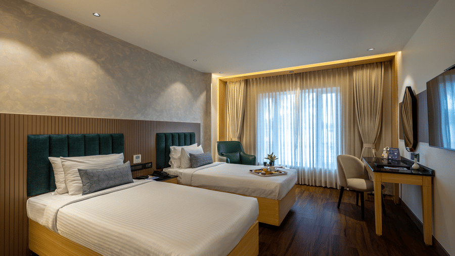 Executive Twin Room at The Citrine, Bangalore, with 2 single beds, green padded headboards, an armchair, work desk, and sheer curtains over the window.