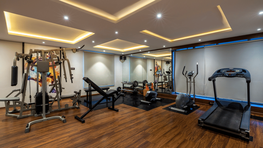 Gym at The Citrine, Bangalore, with a multi-station weight machine, adjustable bench, dumbbells, elliptical trainer, and a treadmill on wooden flooring.