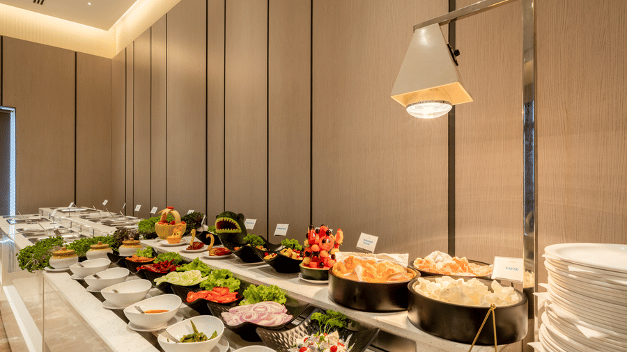 Hotel buffet spread featuring long table lined with variety of dishes in chafing pots under a heat lamp.