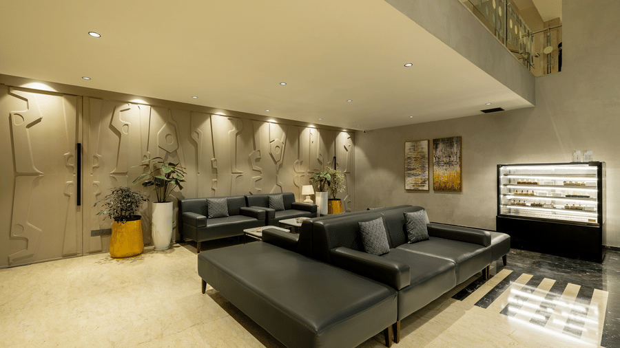 Hotel Reception area at The Citrine, Bangalore, featuring dark sectional sofas, tall planters, and a large display screen in a spacious lobby.