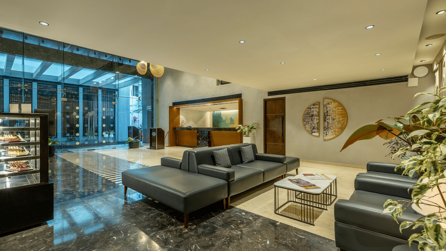 Reception lounge at The Citrine, Bangalore, with grey leather sofas, a metal coffee table, marble flooring, and a pastry display case nearby.