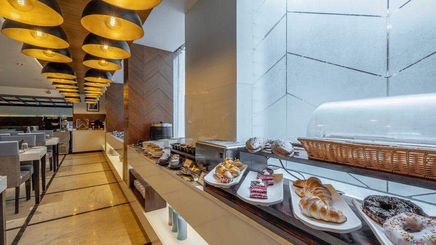 Restaurant counter at The Citrine, Bangalore, displaying pastries, croissants, and donuts on white platters beneath black-and-gold pendant lights.