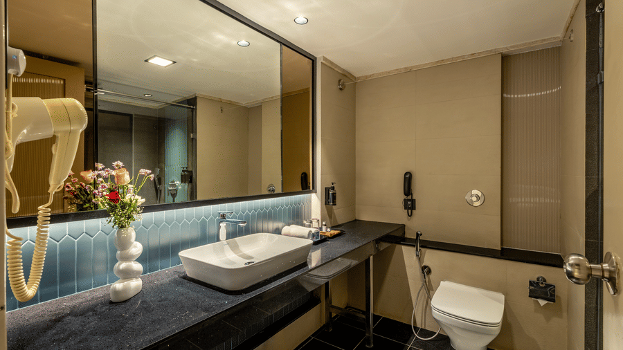 Restroom  featuring a wash basin, a bathroom mirror, a flower vase, and a commode at The Citrine, Bangalore.
