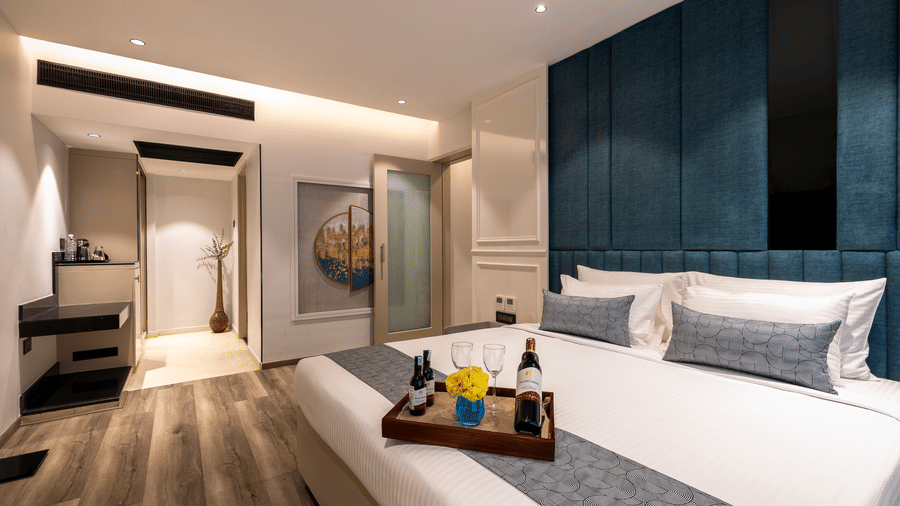 Spacious hotel room showing a neatly made bed, a decorative teal wall panel, and a view of the room's entryway at The Citrine, Bangalore.