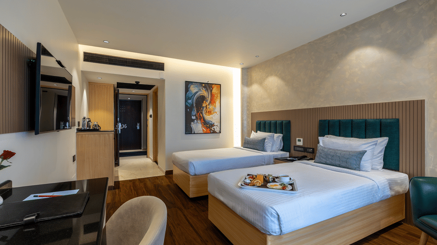 A guest room with two single beds, teal headboards, and a television mounted on the wall at The Citrine, Bangalore.
