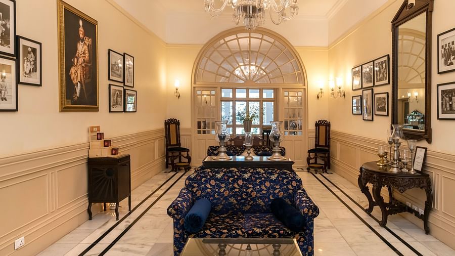 The lobby of The Claridges Nabha Residence in Mussoorie, featuring sofas, wall paintings, a chandelier, a mirror, and various decorative items.