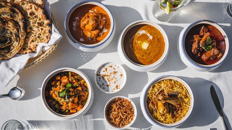 A white dining table set with various bowls of dal, biryani, curd, chicken, and other dishes 
