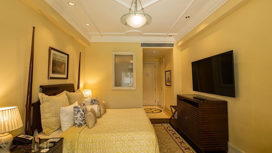 Side view of the Deluxe King Bed Room Pool View at The Claridges New Delhi, featuring a cosy king sized bed, wall-mounted TV, and bedside lamps
