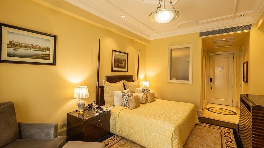 Side view of the Deluxe King Bed Room Pool View at The Claridges New Delhi, featuring a cosy king sized bed, wall-mounted TV, and bedside lamps