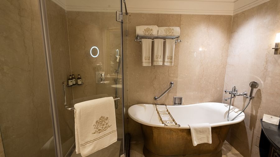 Washroom of the Grand Luxury King Bed Room at The Claridges New Delhi, featuring a stylish bathtub, glass-enclosed bath area, and a neatly hung towel on the wall