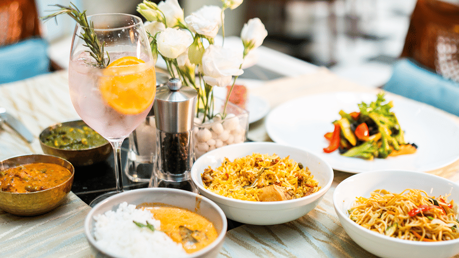 Elegant brunch spread with gourmet dishes, including biryani, curry with rice, stir-fried noodles, and grilled vegetables, served with a refreshing citrus cocktail