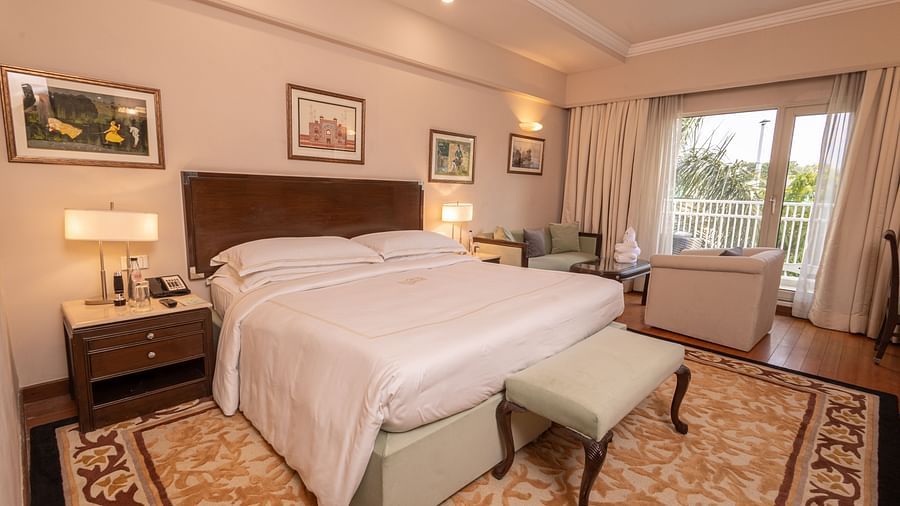 Luxury King Bed Room with Balcony at The Claridges New Delhi, featuring a cosy king sized bed with bedside lamps and a scenic view through a large window