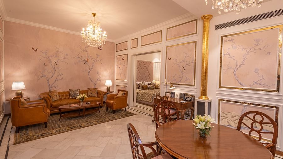 Luxury Suite at The Claridges New Delhi, featuring a large corner sofa, an elegant dining table, and a chandelier hanging overhead