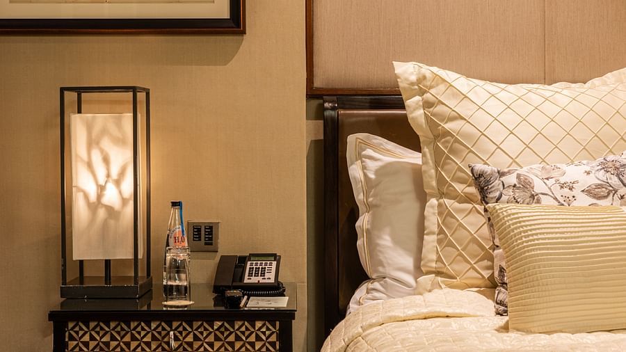 a closeup shot of the side table besides the bed featuring a night lamp and the soft pillows on the bed at the cabana room - The Claridges New Delhi