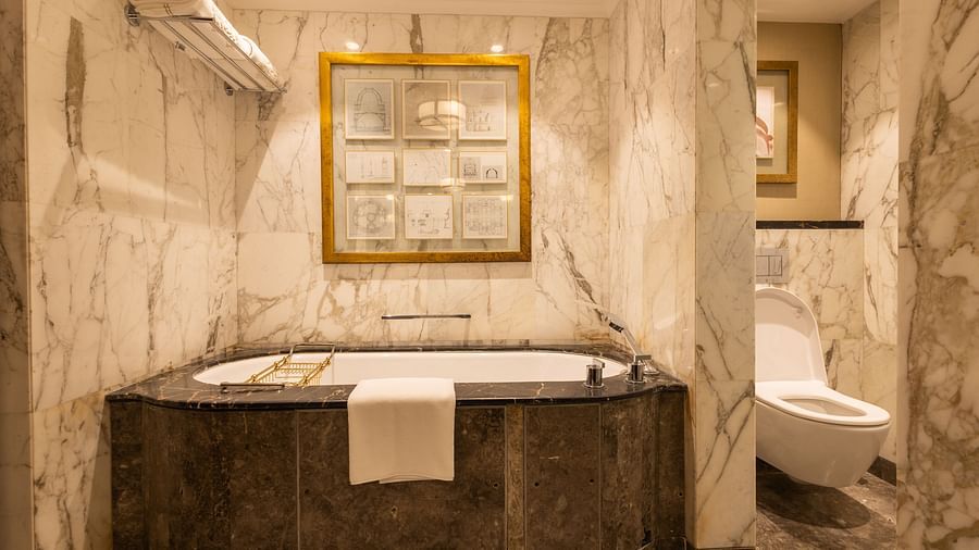 image of a luxurious bathtub with a huge golden photo frame over it at our cabana room - Image of the Cabana Room showcasing exquisite interiors, including a king-size bed and a stylish blue seating area positioned in front of the bed at The Claridges New 