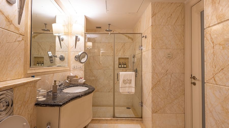 image of a bathroom with a built in cubical shower and a small sink and a square mirror above it - The Claridges New Delhi