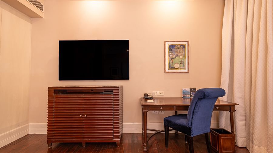 image of a wall mounted television and a work desk with a blue chair at the heritage room - The Claridges New Delhi