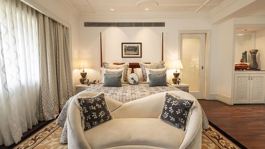 image of plush king size bed along with a white couch in front of it at our viceroy house estate suite - Two chairs, accompanied by a small coffee table, are placed in the middle of the room at The Claridges New Delhi. 