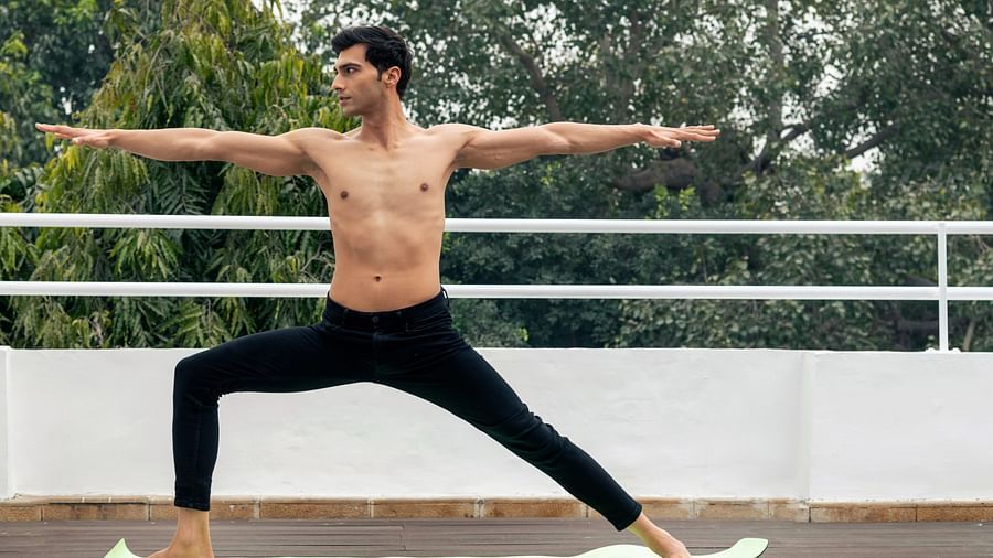A person striking a yoga pose with trees in the background - The Claridges New Delhi
