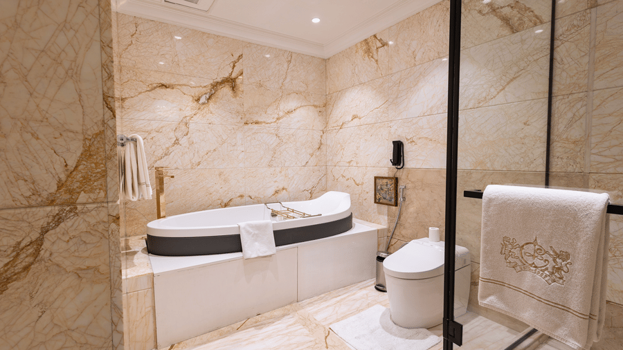 Presidential Suite bathroom featuring marble walls and flooring, a freestanding bathtub, glass enclosed shower, and vanity area at The Claridges New Delhi.