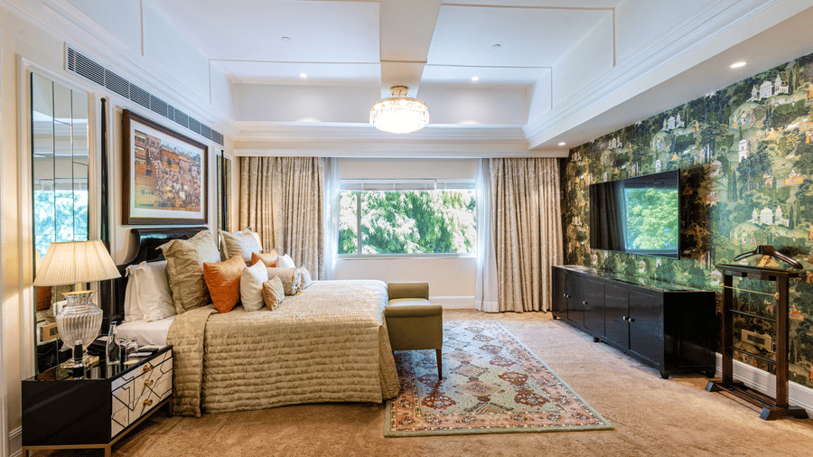Presidential Suite bedroom featuring a sofa, armchair, coffee table, television, floor lamp, and large windows overlooking greenery at The Claridges New Delhi.