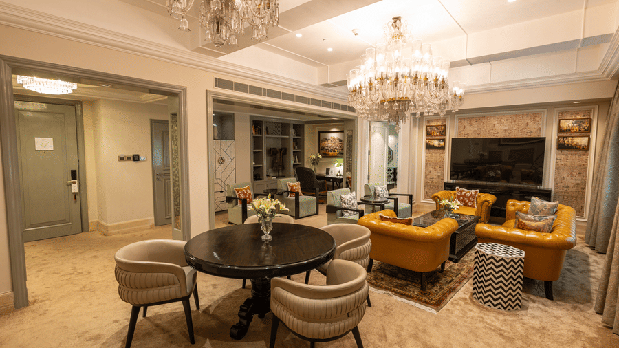 The living area of Presidential Suite featuring a round coffee table, upholstered armchairs, a sofa, floor lamp, and chandelier at The Claridges New Delhi.