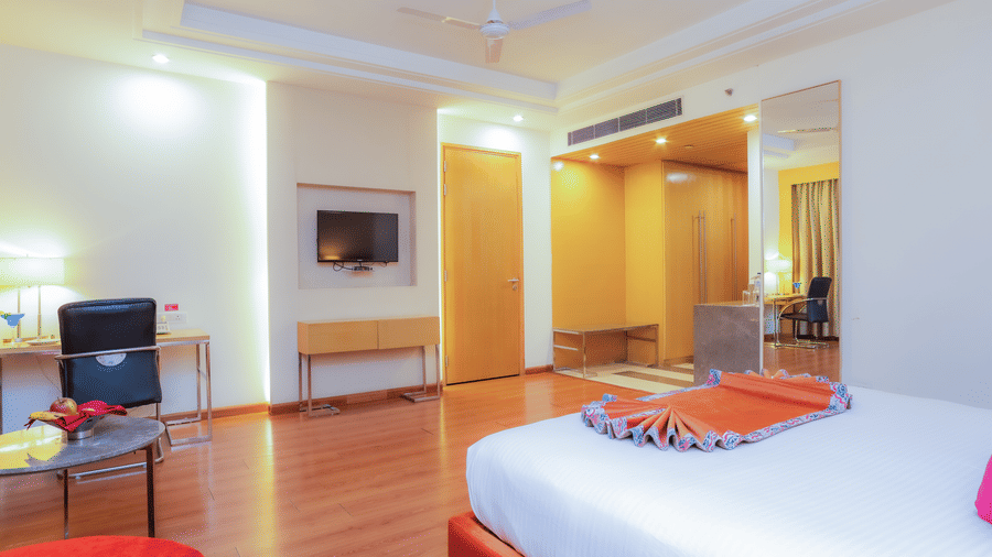 A bright hotel room featuring a comfortable bed and modern furnishings, viewed from the corner at The Conway, Meerut.