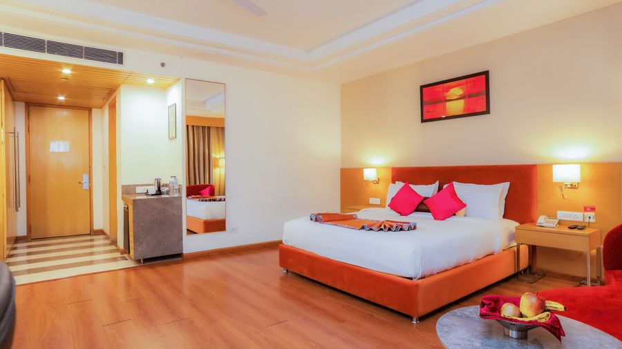 A welcoming hotel room showing the bed, a fruit bowl, and a luggage trolley near the entrance at The Conway, Meerut.