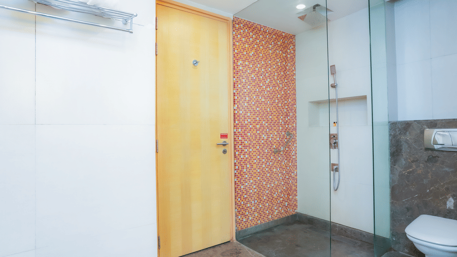 A well-designed hotel bathroom entrance with a glass shower enclosure and toilet visible at The Conway, Meerut.